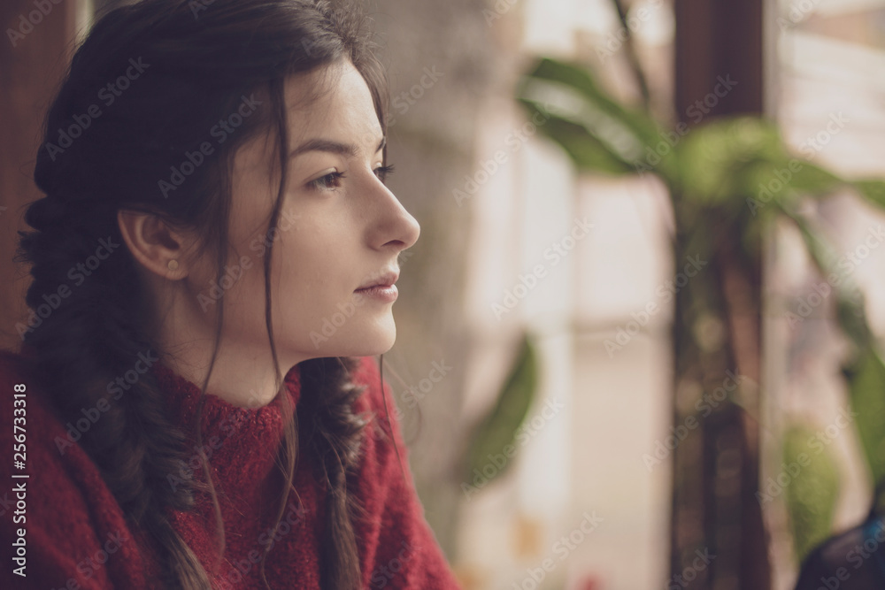Portrait of young beautiful cute cheerful girl dressed in an orange warm sweater and sitting at a table in a cafe at the table near the window Portrait of young beautiful cute cheerful girl dressed in an orange warm sweater and sitting at a table in a cafe at the table near the window