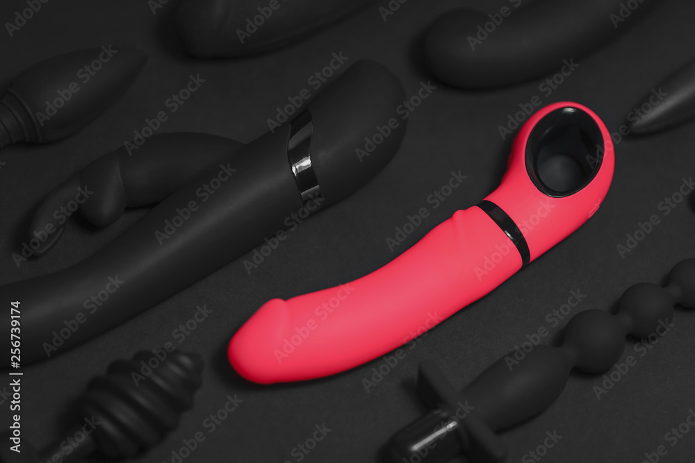 Erotic pleasure toys on a black background. Sex gadgets and masturbation devices. Pink dildo surrounded by black rubber and silicone sex toys: anal butt plugs, vibrators, vaginal balls. Top view. Erotic pleasure toys on a black background. Sex gadgets and masturbation devices. Pink dildo surrounded by black rubber and silicone sex toys: anal butt plugs, vibrators, vaginal balls. Top view.