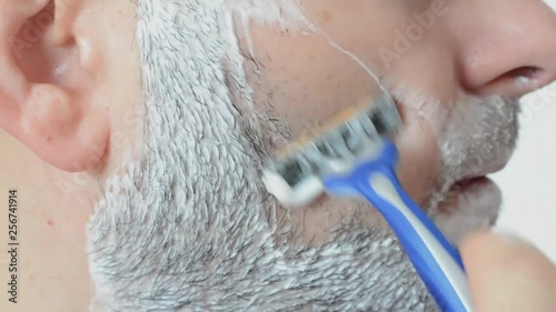Caucasian  man shaving  his beard with a razor ..