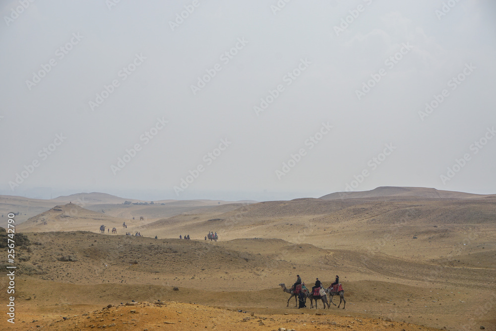 Giza, Egypt: Tourists ride camels on the sand near the Khufu Pyramid Complex. Giza, Egypt: Tourists ride camels on the sand near the Khufu Pyramid Complex.