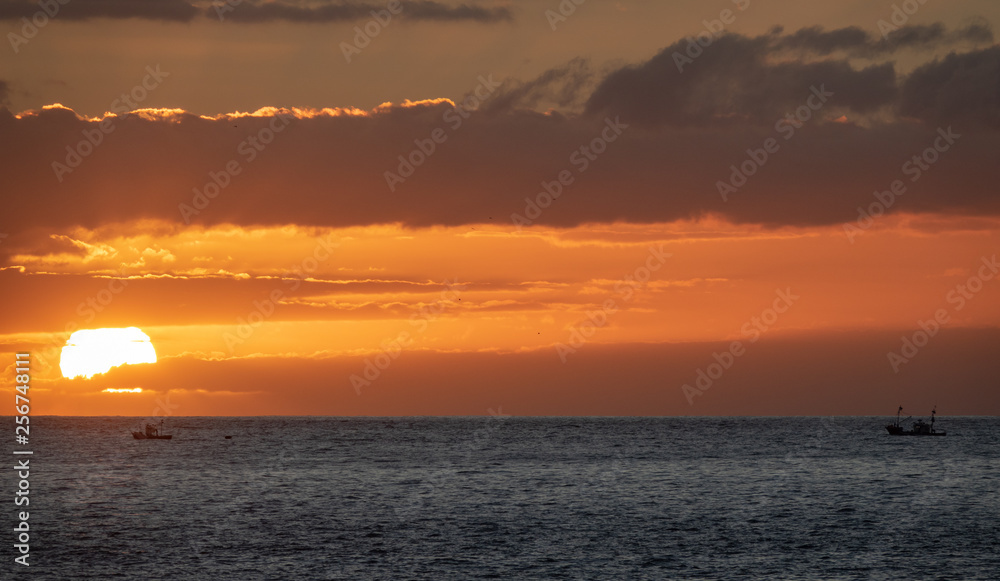 Sunset over the ocean with two small fishing boats