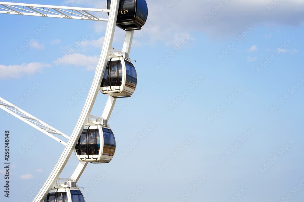 Part of white ferris wheel against blue cloudy sky background. Close-up of swirling big wheel against of blue cloudy sky Part of white ferris wheel against blue cloudy sky background. Close-up of swirling big wheel against of blue cloudy sky