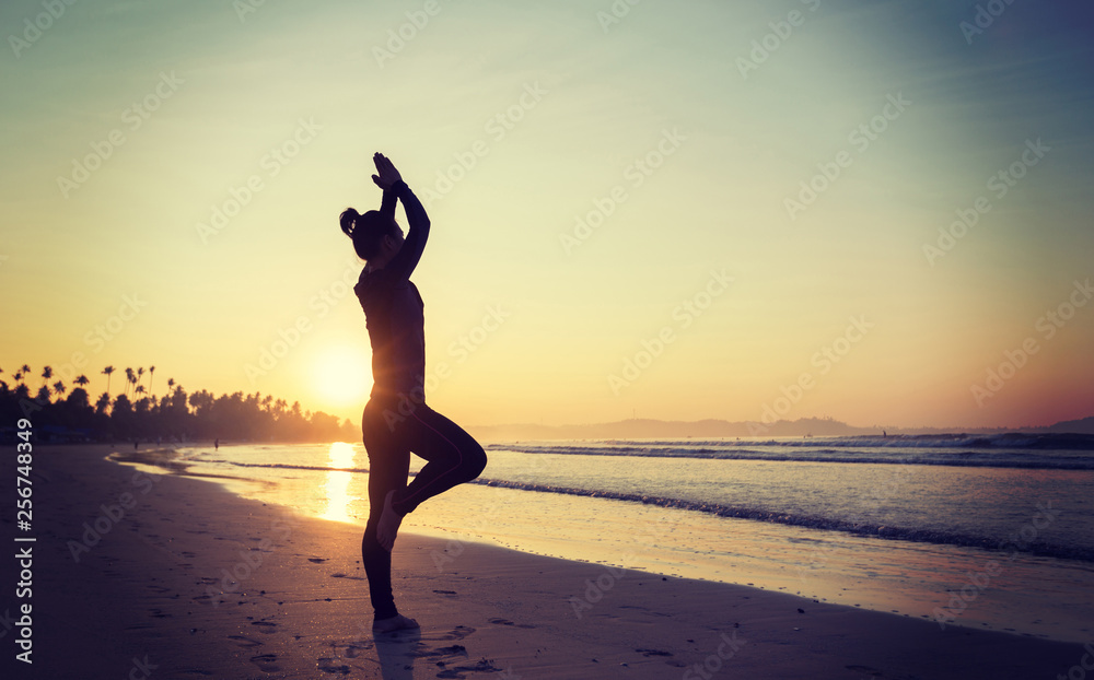 Woman practicing yoga on sunrise beach