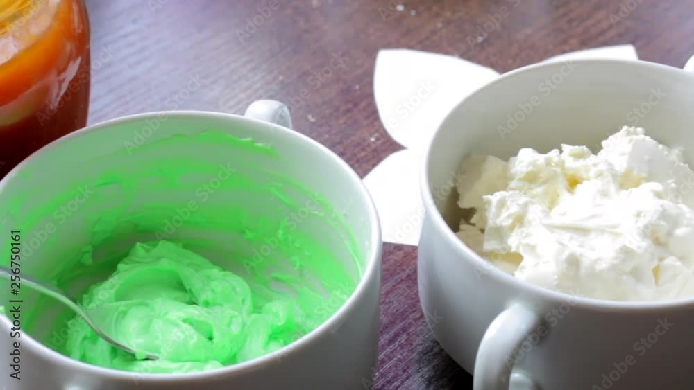 Woman preparing cream for making cakes. Mixes cream cheese and food coloring. Nearby is a jar of jam.. Woman preparing cream for making cakes. Mixes cream cheese and food coloring. Nearby is a jar of jam..