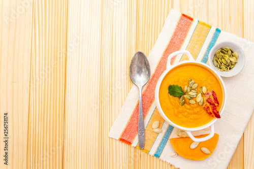 Pumpkin cream soup. White ceramic bowl with fresh pumpkin, dry pumpkin seeds, smoked bacon, herb. With vintage linen cloth (napkin) on wooden background, top view