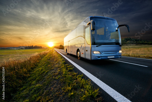 Bus traveling on the asphalt road in rural landscape at sunset