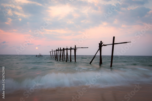 The old and broken wooden bridge on the beach with sunset