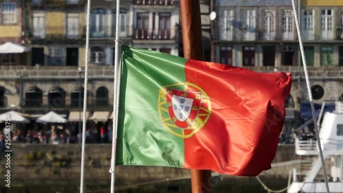 Portuguese national flag flying in slow motion from the mast of a traditional boat on Douro river in Porto, Portugal.