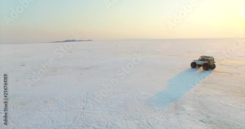 White swamp buggy is driving on ice of big beautiful frozen lake Hanka in the evening. Aerial. Far East of Russia photo