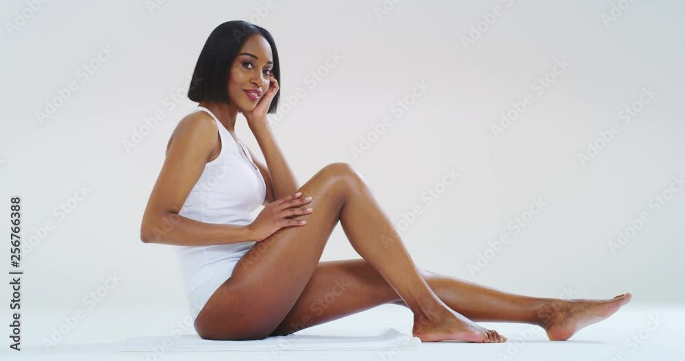 Slow motion of young dark skin woman with perfect body touching gently her hairless soft and silky legs after depilation isolated on a white background. 
