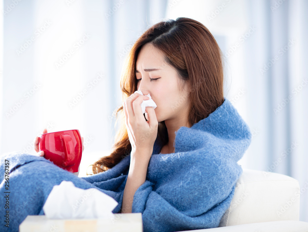 sick woman blowing her nose while sitting on the sofa sick woman blowing her nose while sitting on the sofa