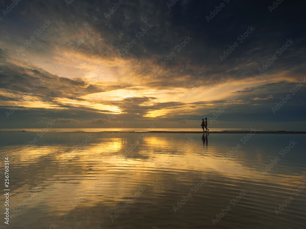 Silhouette couple walking on beach during sunrise ,Reflection of in the calm sea.