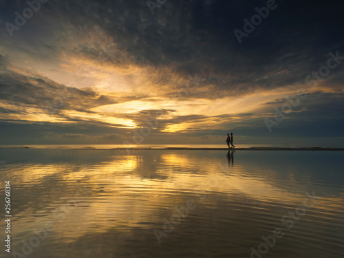 Silhouette couple walking on beach during sunrise ,Reflection of in the calm sea. © Thapanon Phoonchai