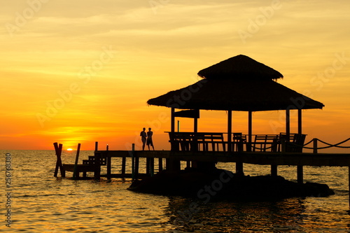 Beautiful Tropical sea with silhouette couples are standing watching the sunset on a wooden bridge.