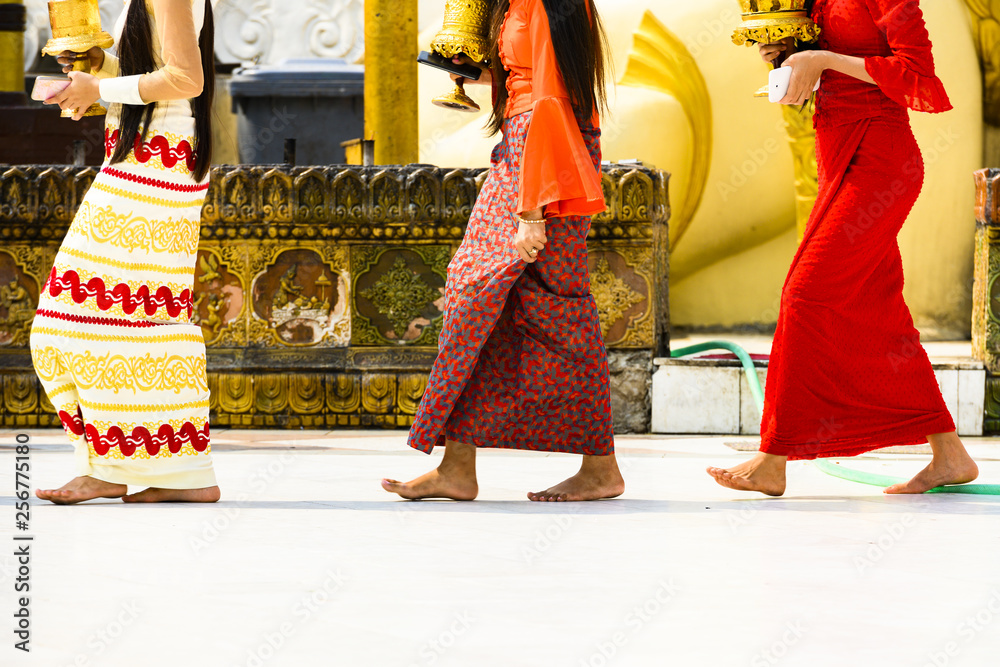 (selective focus) Some Burmese Buddhist faithful are walking barefoot around the Shwedagon Pagoda wearing a traditional and colorful Longyi (traditional Burmese clothes). Yangon, Myanmar. - obrazy, fototapety, plakaty 