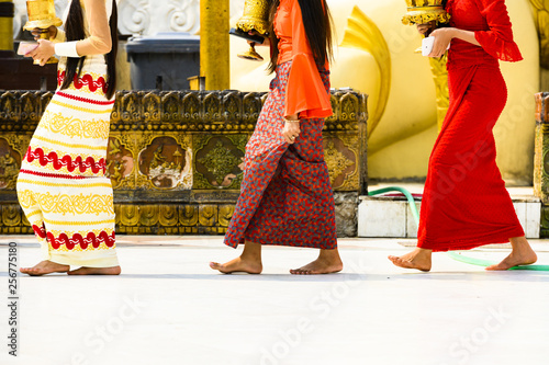 Obraz na płótnie (selective focus) Some Burmese Buddhist faithful are walking barefoot around the Shwedagon Pagoda wearing a traditional and colorful Longyi (traditional Burmese clothes). Yangon, Myanmar. w salonie