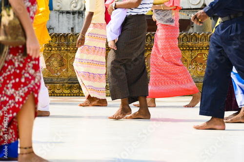 (selective focus) Some Burmese Buddhist faithful are walking barefoot around the Shwedagon Pagoda wearing a traditional and colorful Longyi (traditional Burmese clothes). Yangon, Myanmar.