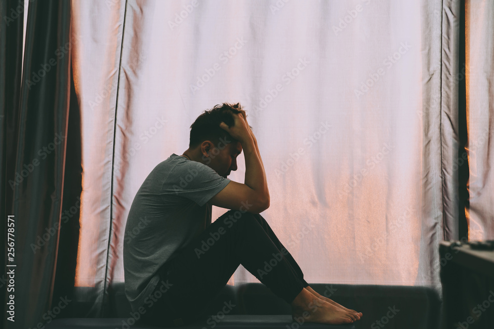 Depressed man sitting on the chair and holding his forehead while having headache in the dark bedroom with low light environment.Depression concept Depressed man sitting on the chair and holding his forehead while having headache in the dark bedroom with low light environment.Depression concept