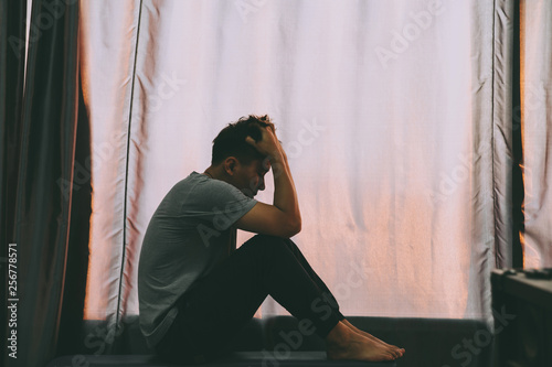 Depressed man sitting on the chair and holding his forehead while having headache in the dark bedroom with low light environment.Depression concept