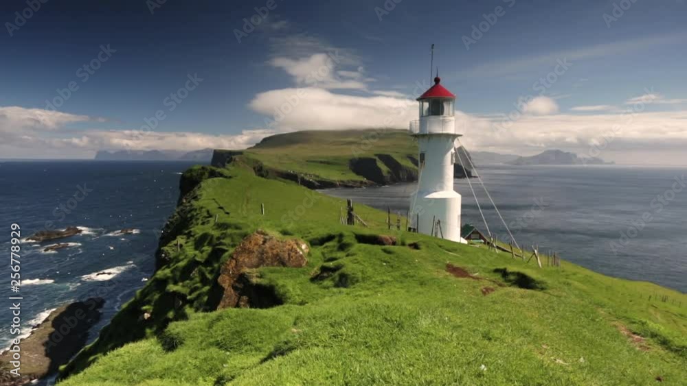 Zoom out shot of white lighthouse standing on grassy nordic island Mykines Zoom out shot of white lighthouse standing on grassy nordic island Mykines