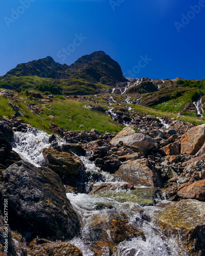 The river flows among the stones from the mountain in the surroundings of Dombai. The Caucasus Mountains on a summer, clear day. Tourie Lake. © dmitriydanilov62
