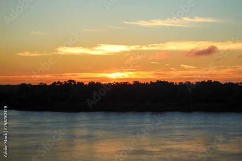 Beautiful deep morning dawn with highlights in the orange rays of the summer sun on a river Volga. Toned in orange colour and backlit.
