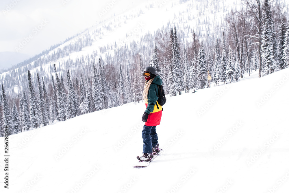 Female snowboarder freerider rides a snowboard on a snowy slope.