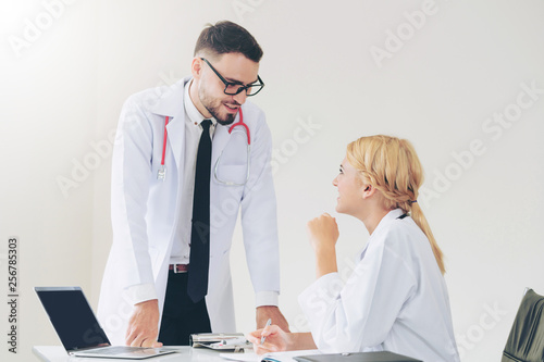 Young female doctor at hospital office having conversation talking with another male doctor standing beside the table. Concept of medical healthcare professional team. photo