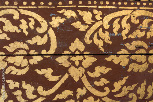 Buddhist hand painted stenciled background in gold with a brown base color - yellow asian pattern on dark red wood texture panels with a worn effect and peeling paint