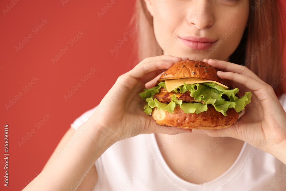 Beautiful young woman with tasty burger on color background, closeup