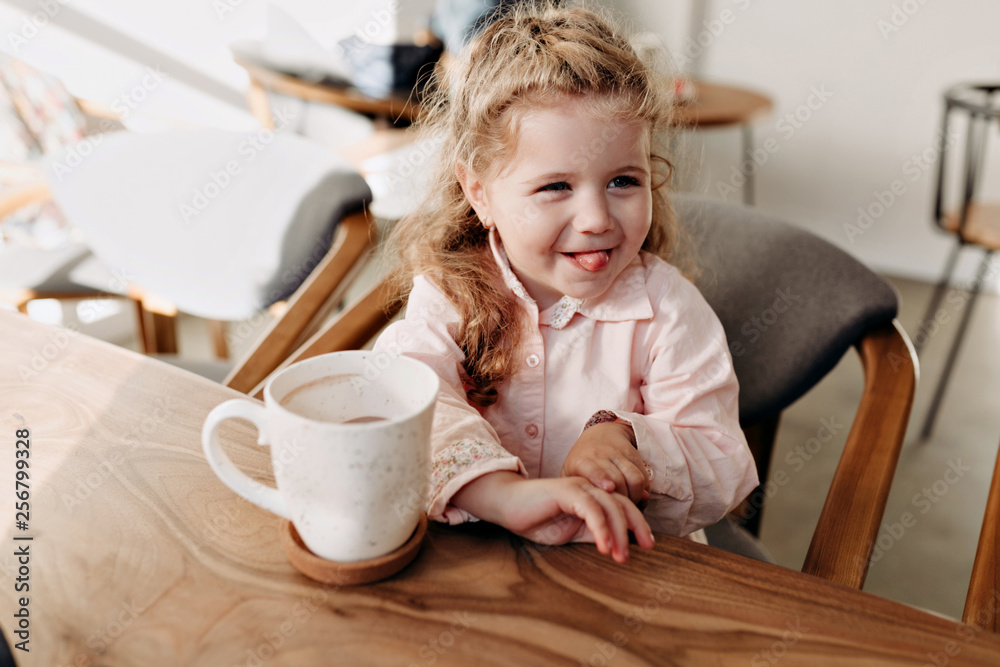 Adorable emotional 5 old years girl with big blue eyes and curls sitting in the big table with cacao Adorable emotional 5 old years girl with big blue eyes and curls sitting in the big table with cacao
