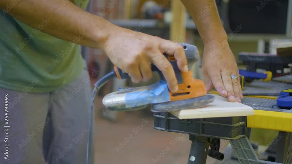 Man sands small piece of wood with hand held power tool. Man sands small piece of wood with hand held power tool.
