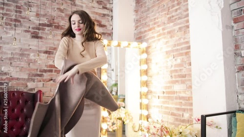 The pretty girl took off her coat and threw it against the background of a large mirror and a brick wall