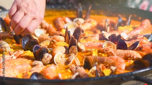 Paella. Person cooking traditional spanish seafood paella with prawns, mussels and fish closeup. Slow motion 4K UHD video footage. 3840X2160 photo