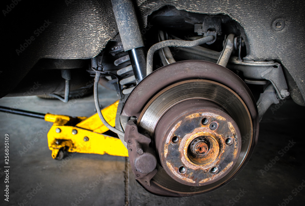 Rusty car disc brake to be maintenance and fixed with the yellow car jack in the garage