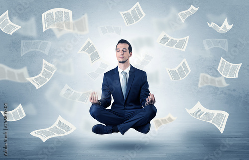 Young businessman meditating with documents and papers flying around him
