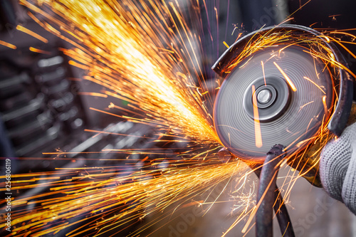 A close-up of a car mechanic using a metal grinder to cut a car bearing in an auto repair shop, bright flashes flying in different directions, in the background tools for an auto repair