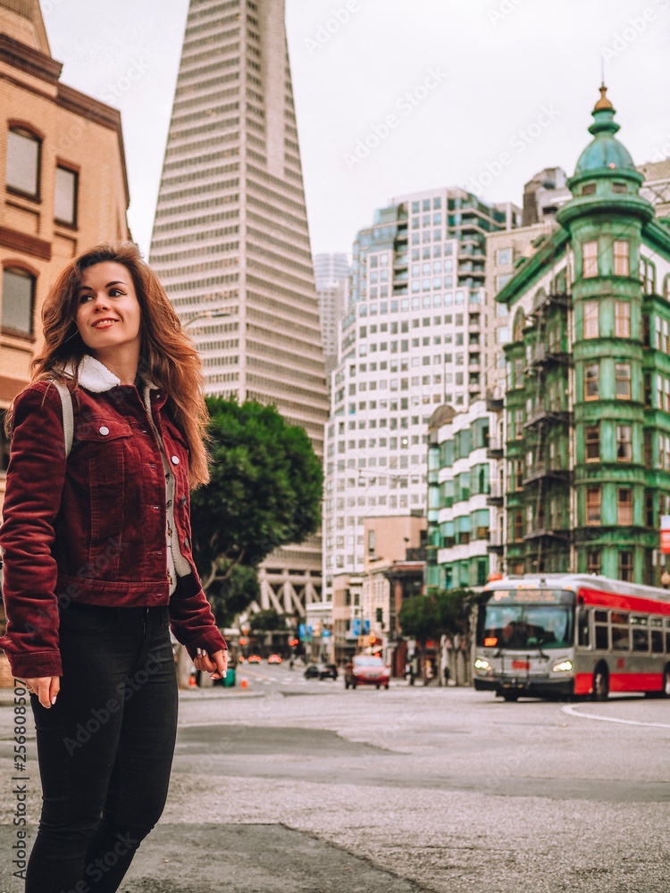 Girl with long hair in a red jacket posing on the streets of San Francisco overlooking the skyscrapers, pyramid tower