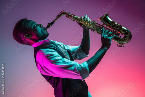 Photography African American handsome jazz musician playing the saxophone in the studio on a neon background