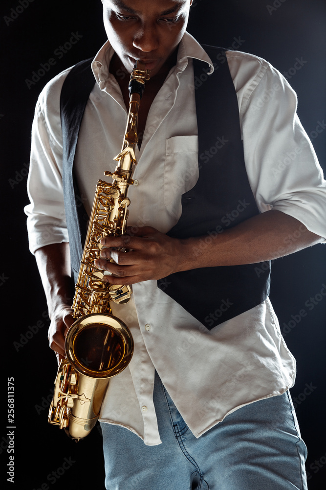 Naklejka premium African American handsome jazz musician playing the saxophone in the studio on a black background. Music concept. Young joyful attractive guy improvising. Close-up retro portrait.