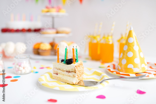 food, celebration and festive concept - piece of cake with candles on plate at birthday party