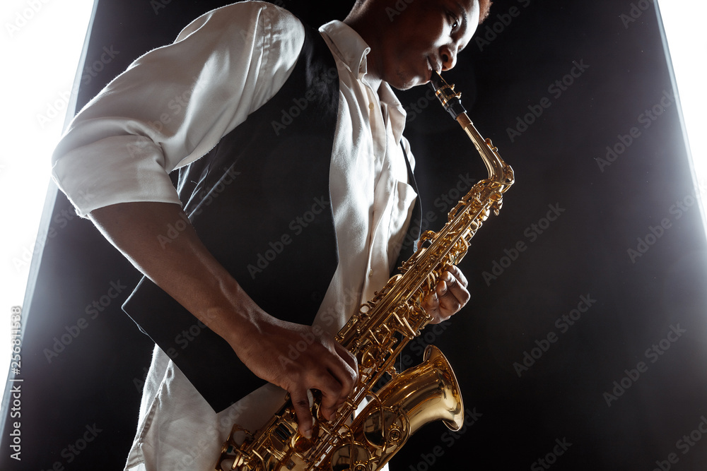 Naklejka premium African American handsome jazz musician playing the saxophone in the studio on a black background. Music concept. Young joyful attractive guy improvising. Close-up retro portrait.