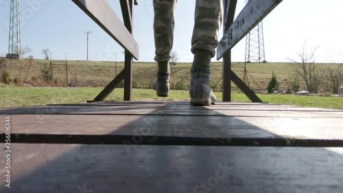 Walking man in camouflage pants and working boots over the wood bridge in the garden at sunny day