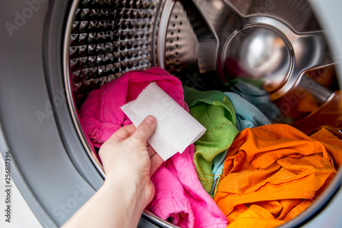 Woman hand put color absorbing sheet inside a washing machine, allows to wash mixed color clothes without ruining colors concept.