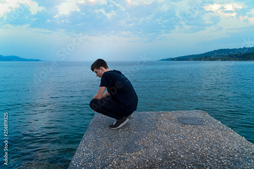 young man crouching on a pier  looking into the sea