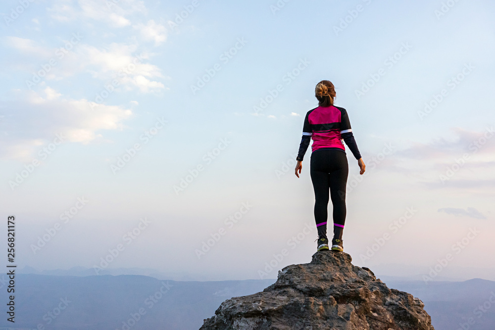 Asian woman in sportswear standing on high rock cliff