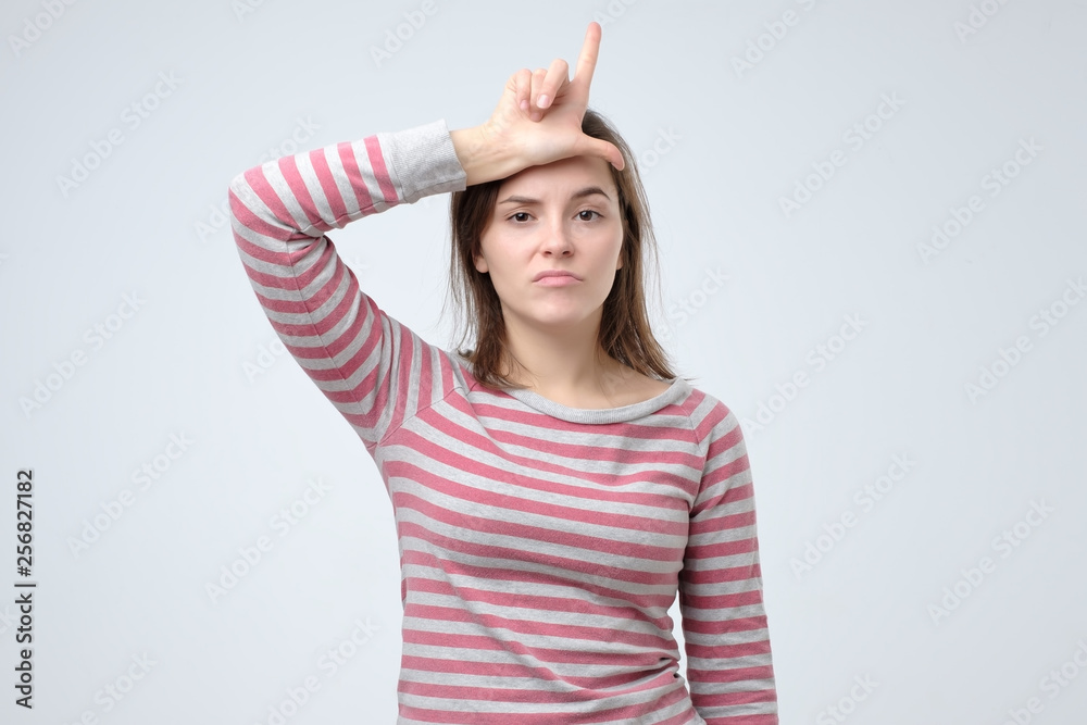 Cheerful young woman showing loser gesture, pointing special sign with fingers Cheerful young woman showing loser gesture, pointing special sign with fingers