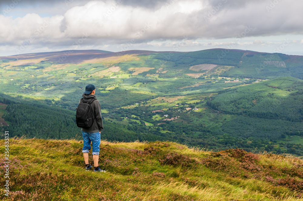 Tourist enjoying the beautiful view and resting on the top of Maulin Peak, Wicklow Mountains, after a hike on a cloudy summer day. 40 shades of green of Ireland.