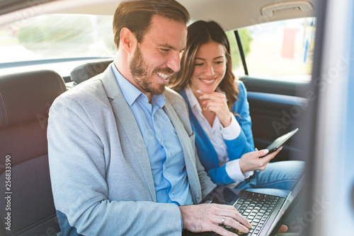 Two young business people driving on a backseat of a car working on laptop and smiling. Successful team businessman and businesswoman.  © srdjanvrebac