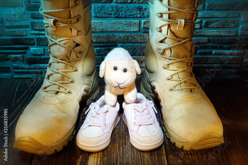 Military army boots and baby shoes.Family and country protection concept.Stone wall in the background